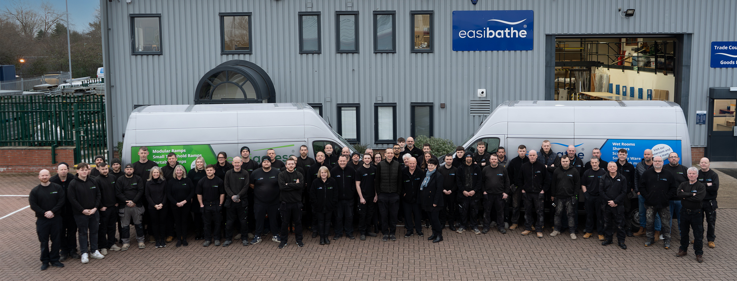All the workers of easibathe stood infront of the easibathe and Easiaccess offices. All in a horse shoe shoe looking toward the camera. 
